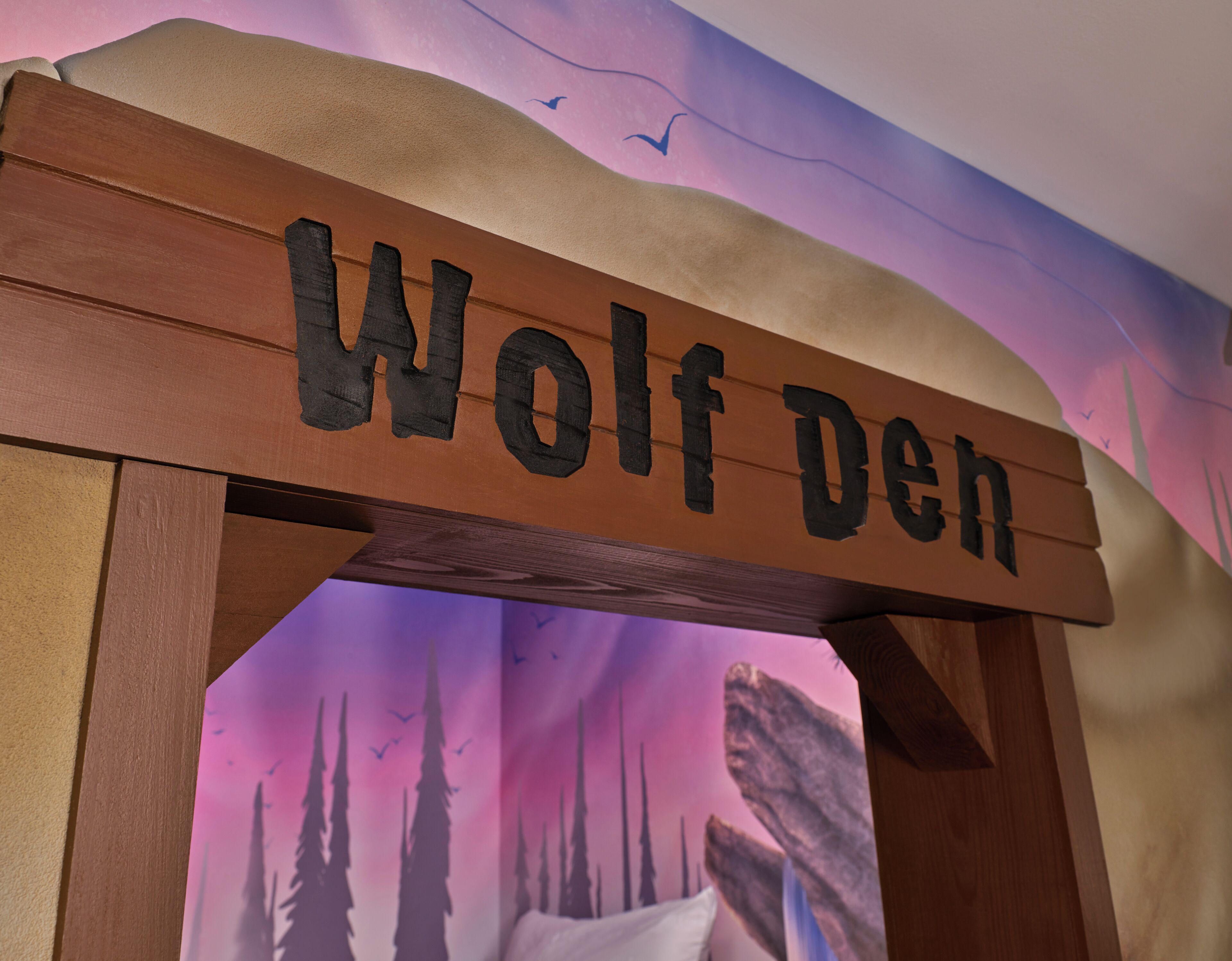 A wooden sign with the text "Wolf Den" against a backdrop of a forest scene.