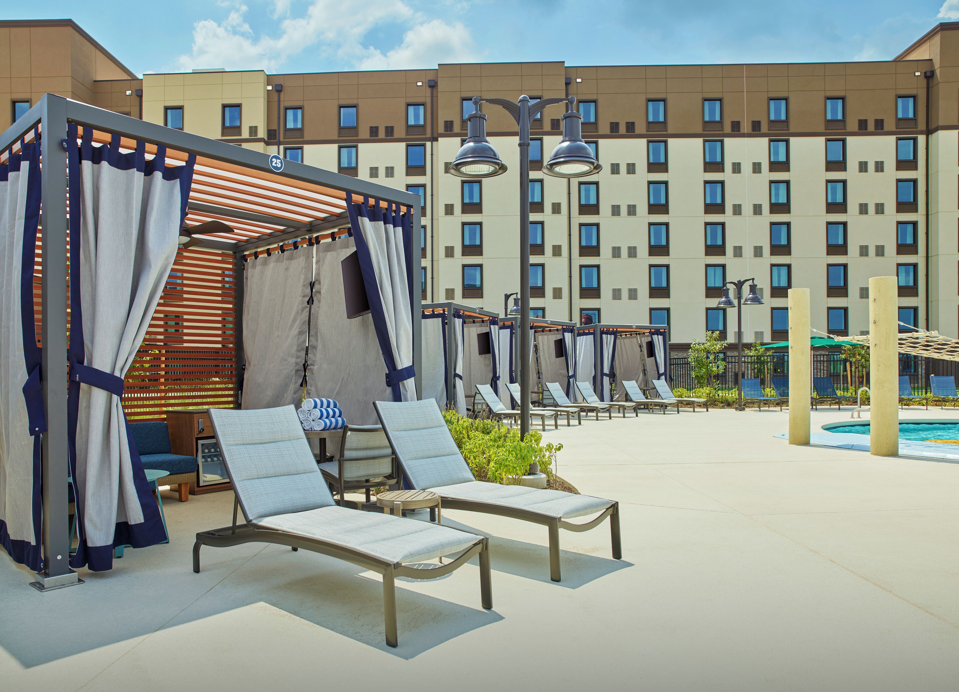 Ein Hotelpoolbereich mit Liegestühlen, einer überdachten Sitzgelegenheit und einem großen Gebäude im Hintergrund.