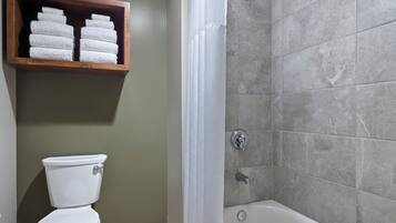 A bathroom with a toilet, a shower with a curtain, and a shelf with towels.