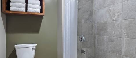 A bathroom with a toilet, a shower with a curtain, and a shelf with towels.