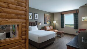 A hotel room with a wooden log wall, a bed, a leather chair, a small table, and a view of the outdoors. - Great Wolf Lodge Webster (Webster)