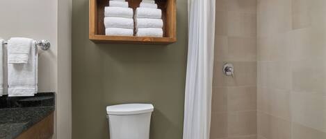 A bathroom with a toilet, a shower with a curtain, and a wooden shelf with towels.