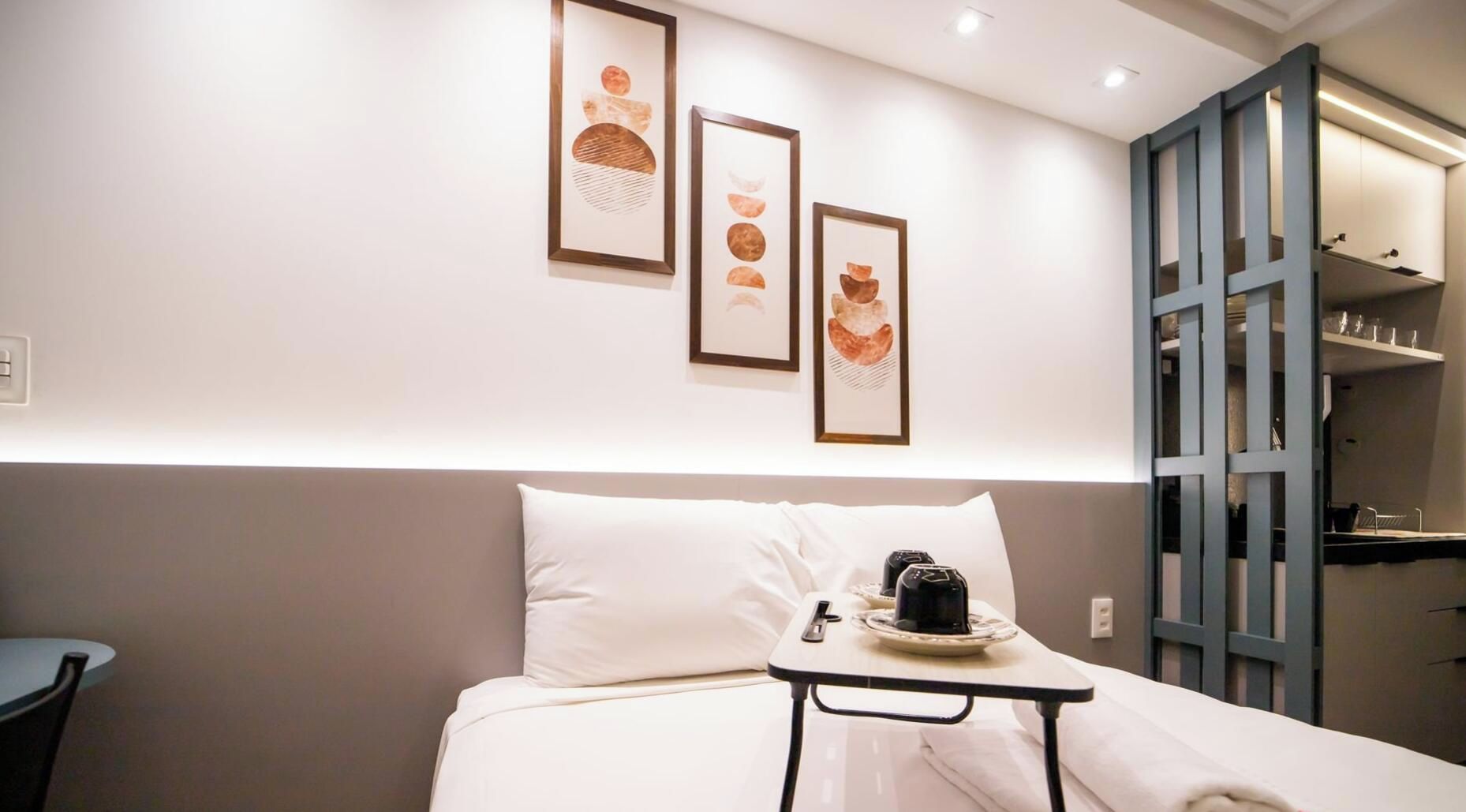 Una habitación de hotel con cama, una mesita con cafetera y obras de arte en la pared.