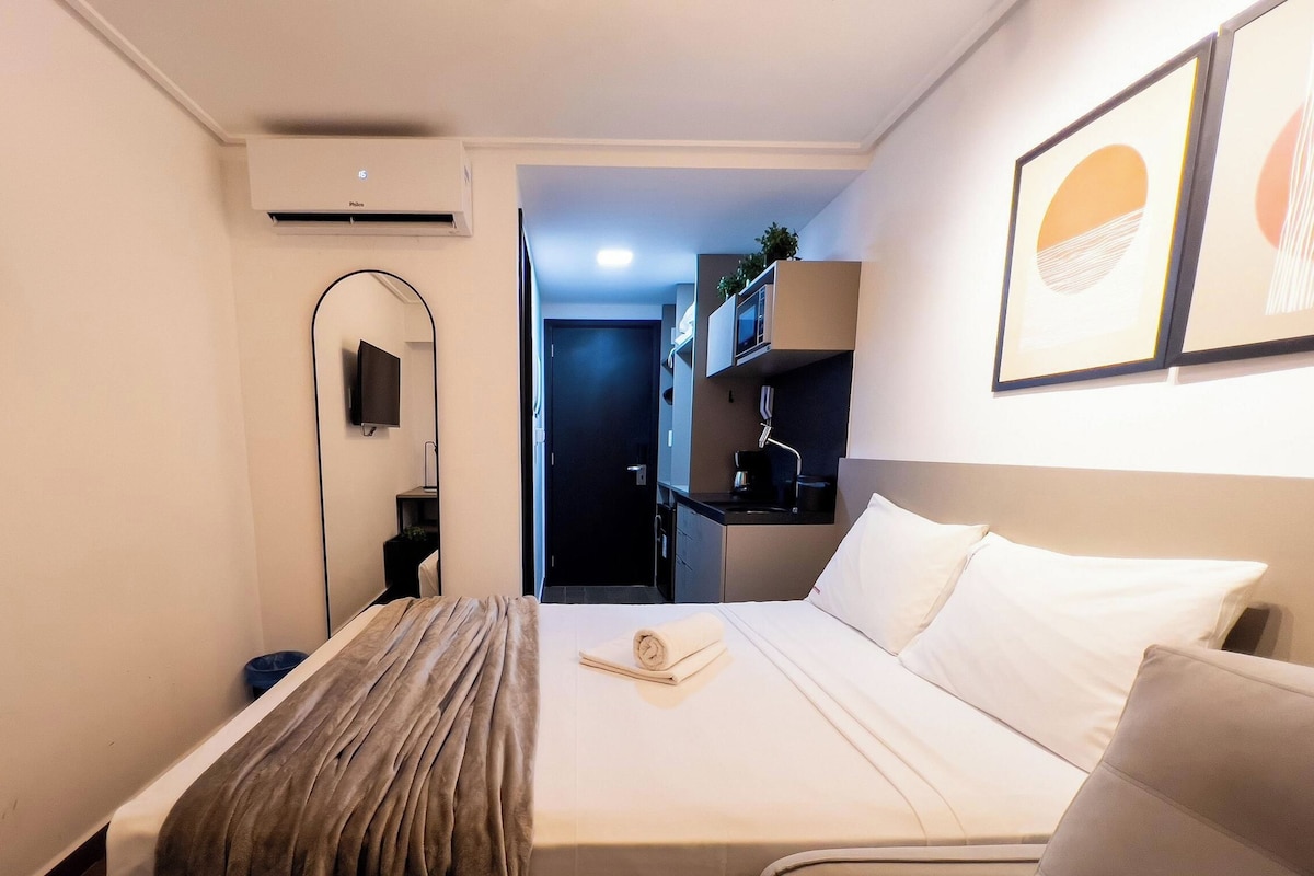 Habitación de hotel con cama, televisor de pantalla plana, espejo y kitchenette.