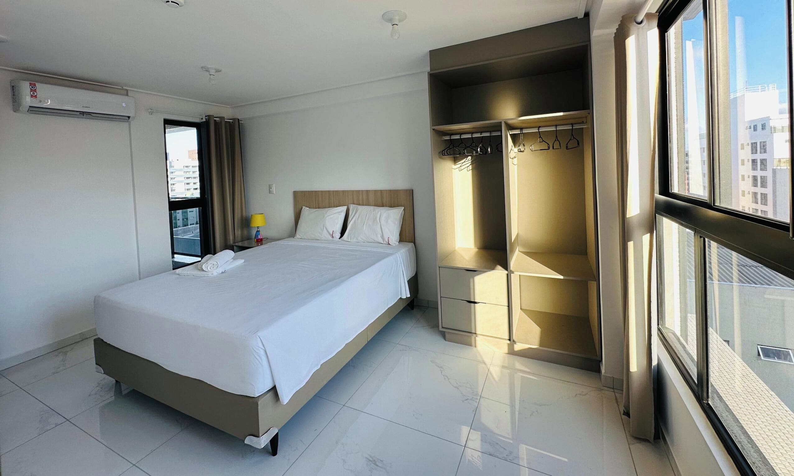 A hotel room with a bed, a wardrobe, and a window with a city view.