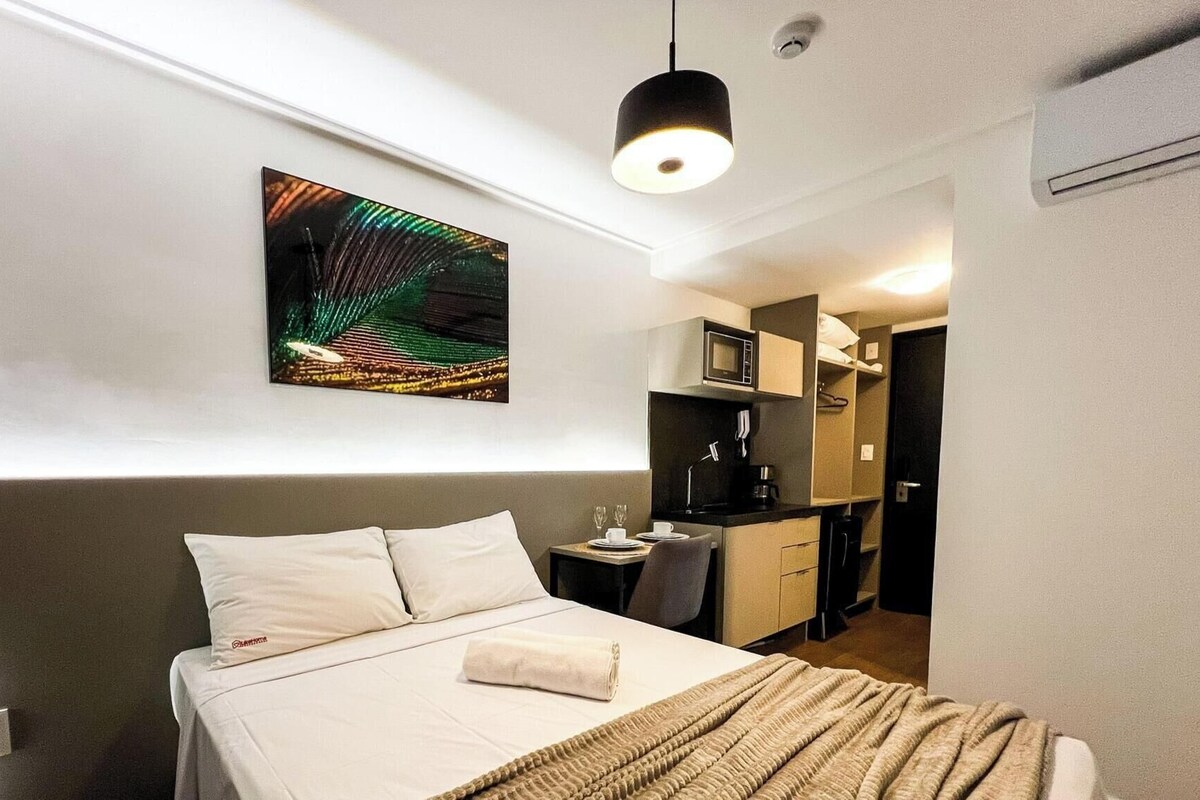 Una habitación de hotel con una cama, un escritorio pequeño, un microondas y un cuadro en la pared.