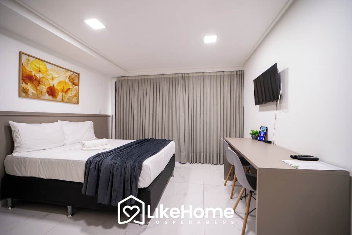 A hotel room with a bed, a desk, a TV, and a painting on the wall.