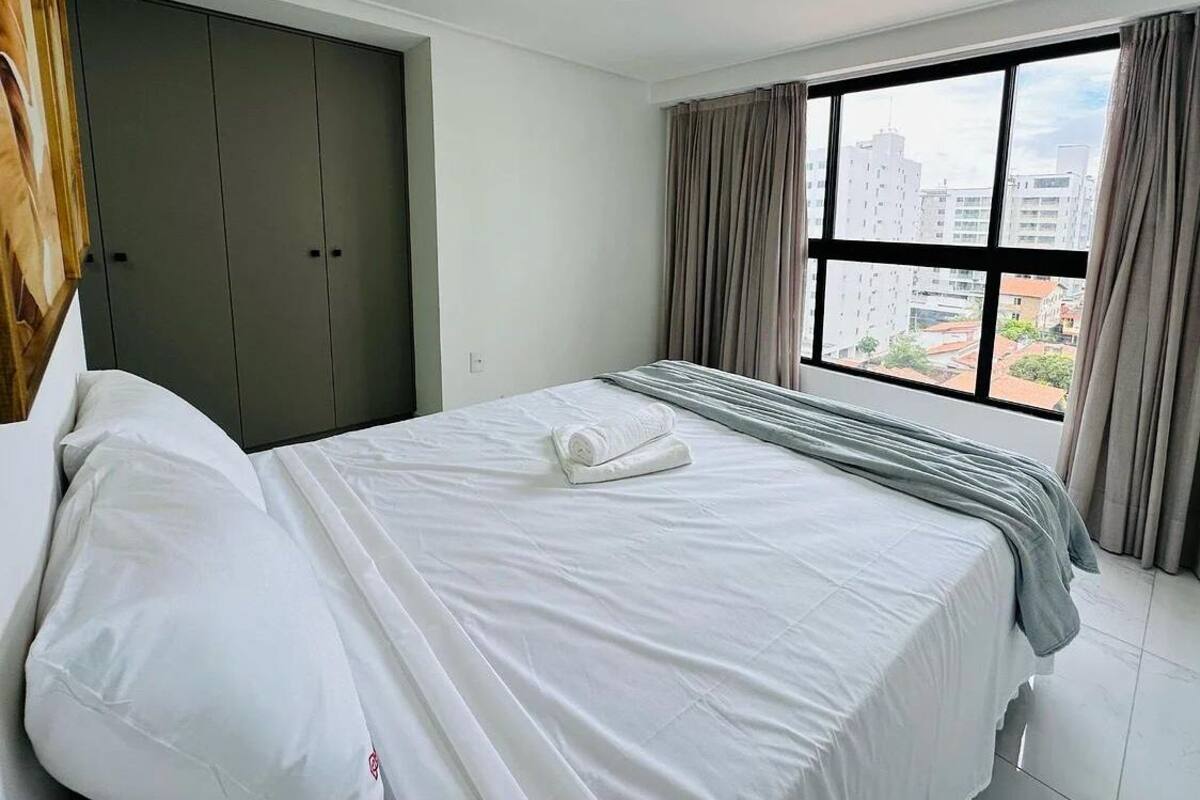 A hotel room with a bed, a wardrobe, and a window with a city view.