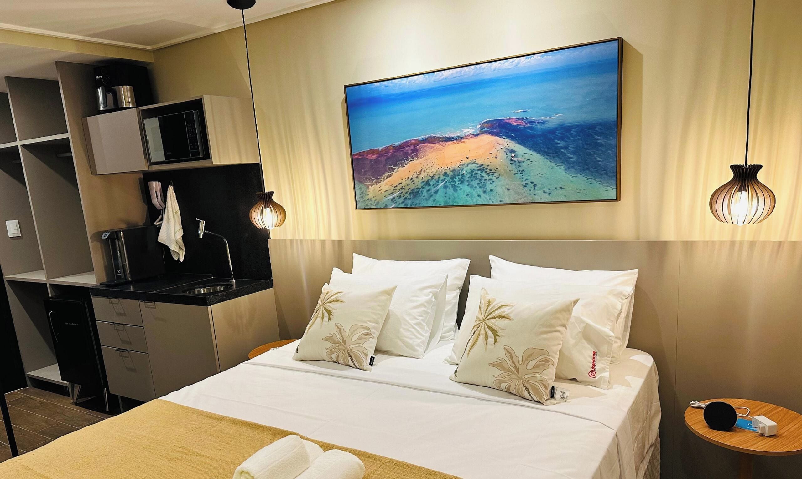 Ein Hotelzimmer mit einem Bett, einem Schreibtisch, einer Mikrowelle, einer Kaffeemaschine und einem Strandbild.