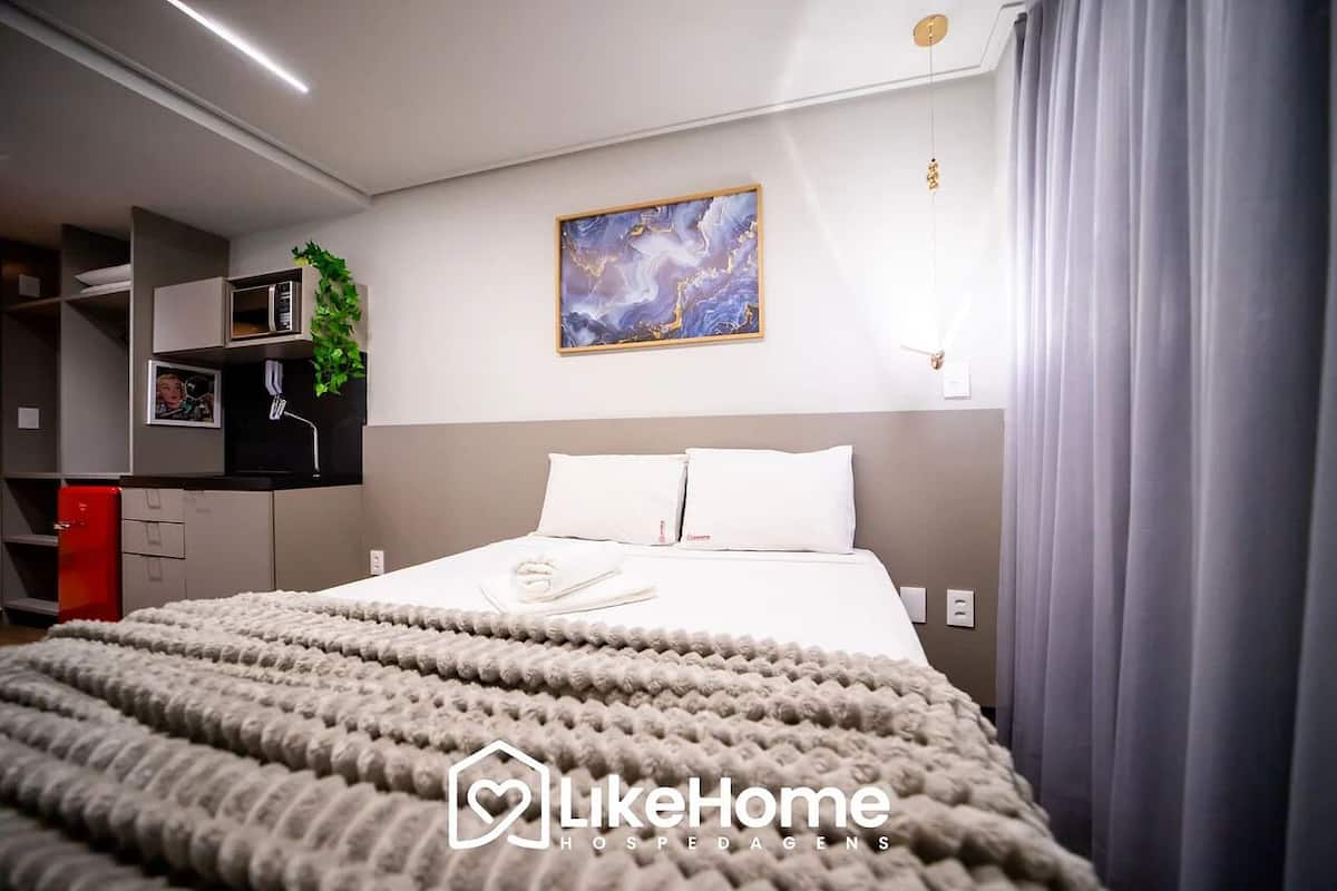 A modern hotel room with a neatly made bed, a painting on the wall, and a small plant on the shelf.