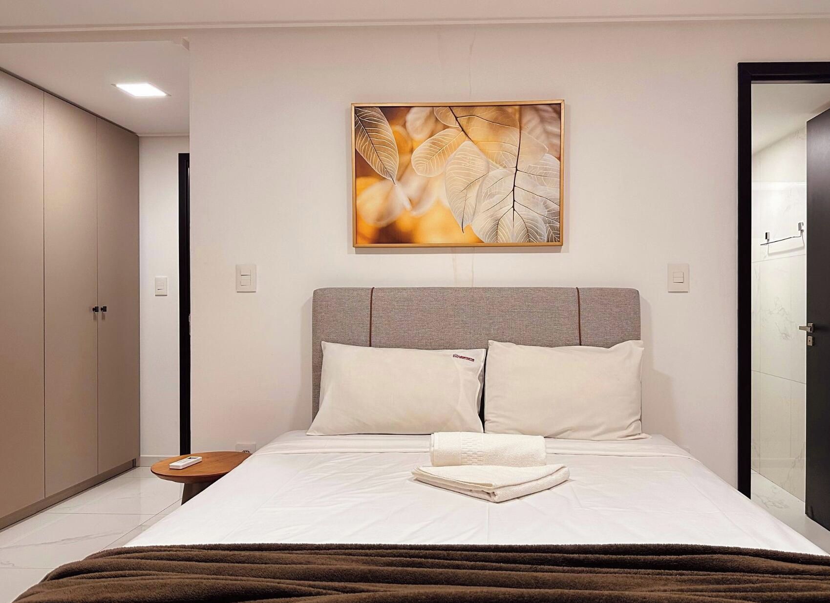 A modern bedroom with a large bed, a nightstand, a wall-mounted artwork, and a wardrobe.