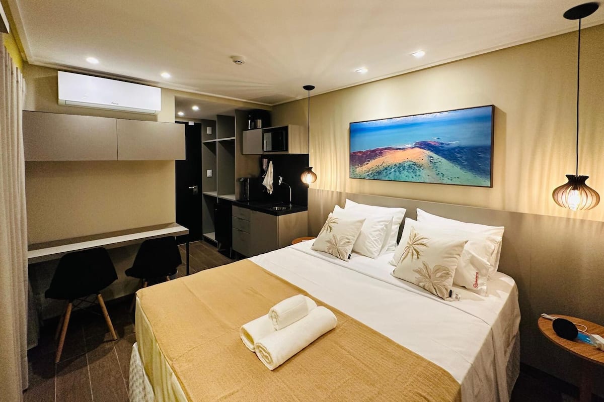 A hotel room with a bed, a desk, a chair, a TV, and a painting on the wall.