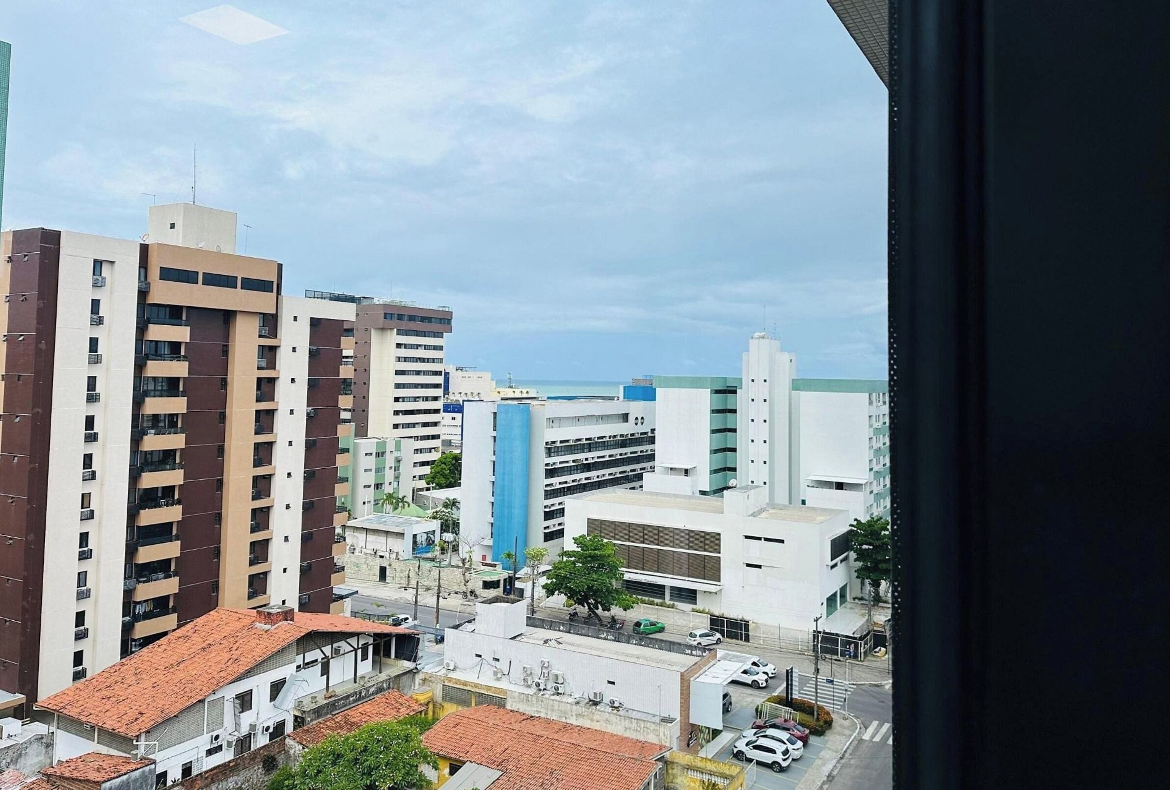 A cityscape with high-rise buildings, a parking garage, and a view of the sea.
