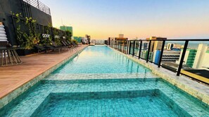 Une piscine sur le toit offrant une vue sur la ville, des chaises longues et une terrasse en bois.