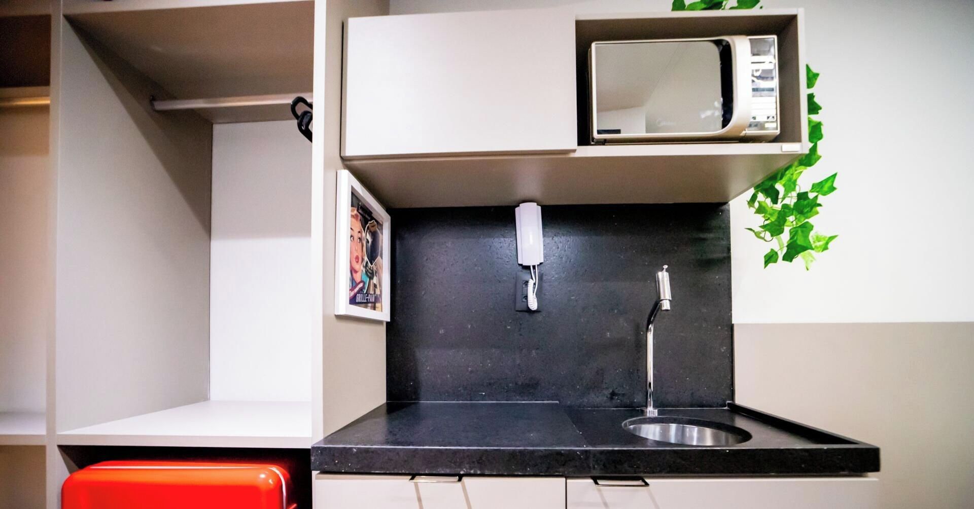 Un angolo cottura compatto con forno a microonde, lavello e piccolo piano di lavoro.