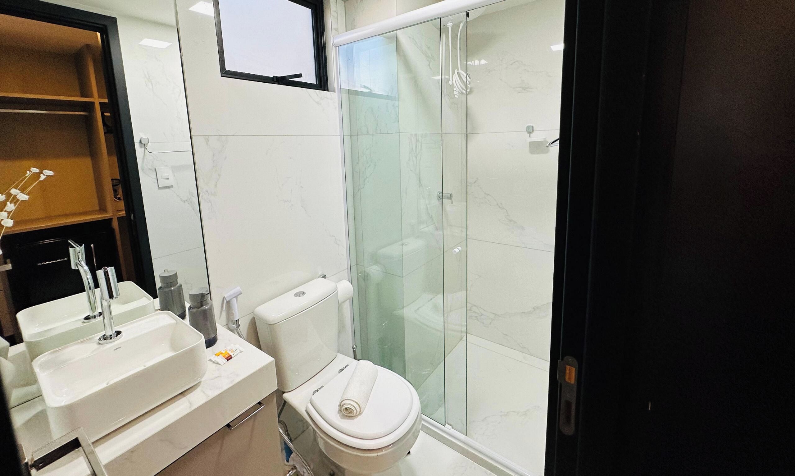Une salle de bain avec une douche à parois de verre, des toilettes blanches et deux lavabos avec des robinets.