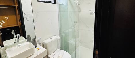 Une salle de bain avec une douche à parois de verre, des toilettes blanches et deux lavabos avec des robinets.