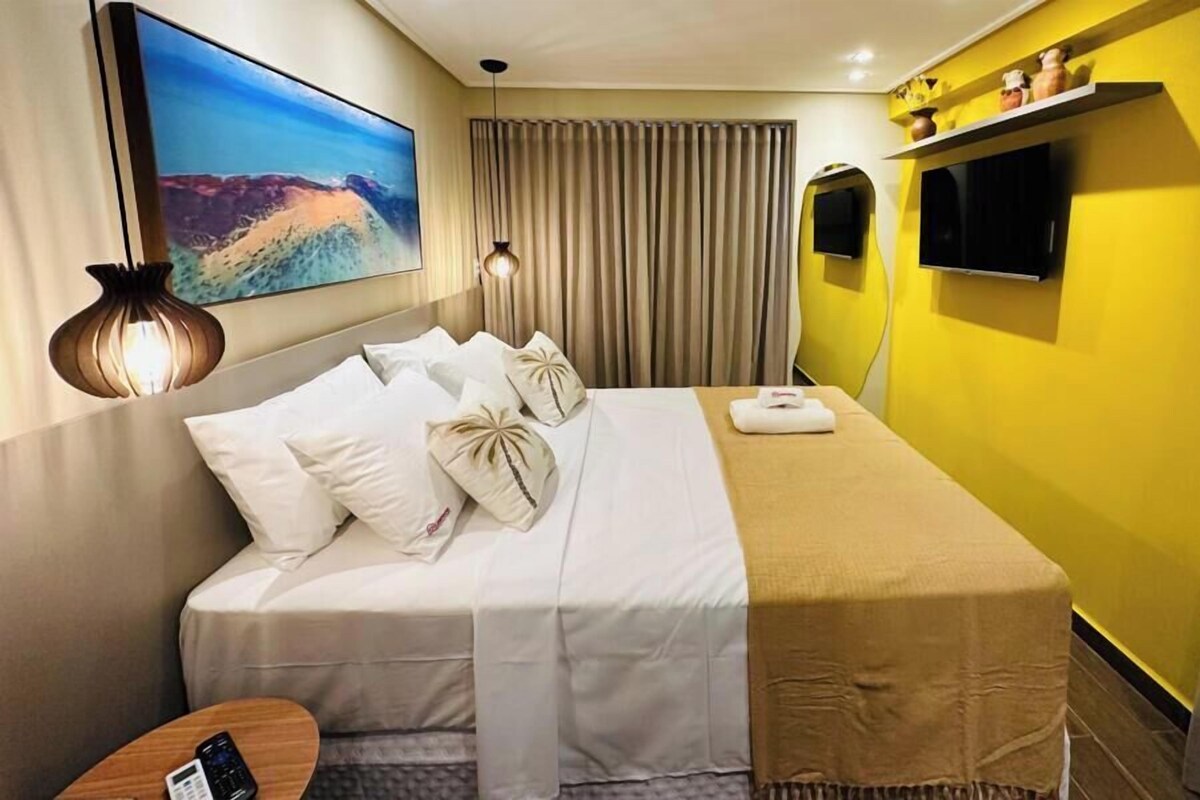 Una habitación de hotel con una cama, un televisor, un cuadro y una cortina.