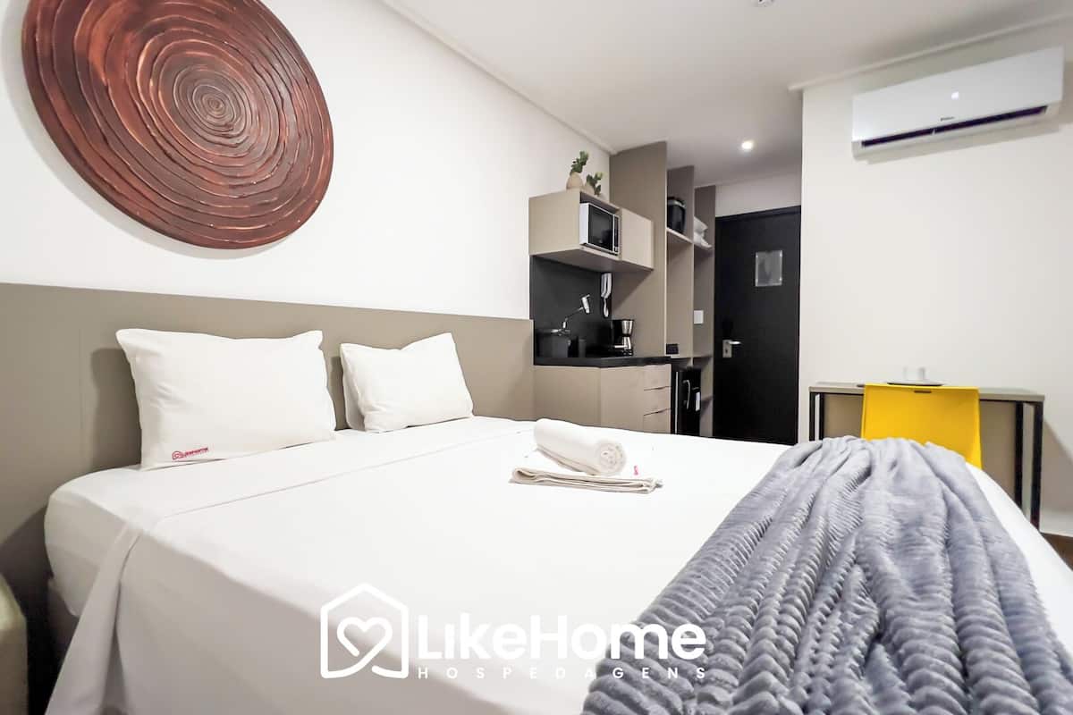 A modern hotel room with a neatly made bed, a small kitchenette, and a bathroom.