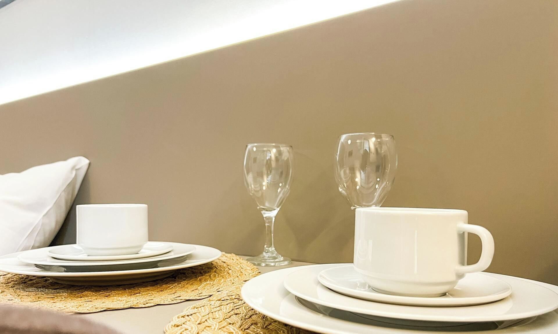 Une table dressée avec une tasse et une soucoupe blanches, un verre à vin et une tasse plus grande, le tout posé sur un set de table en fibres tressées.