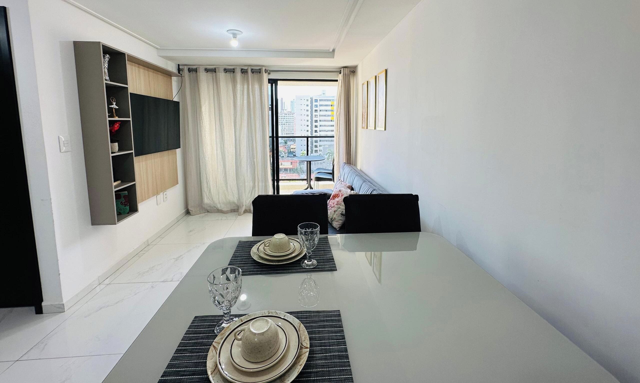 A modern dining area with a glass table, black placemats, and a view of the city through large windows.