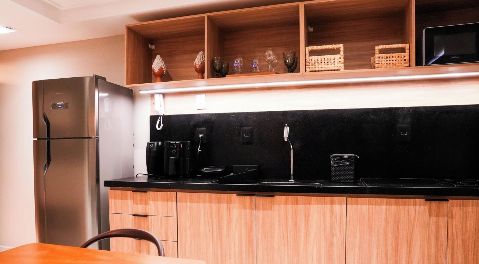 Una cucina con frigorifero in acciaio inossidabile, un piano di lavoro nero, mobili in legno e un forno a microonde sullo scaffale.