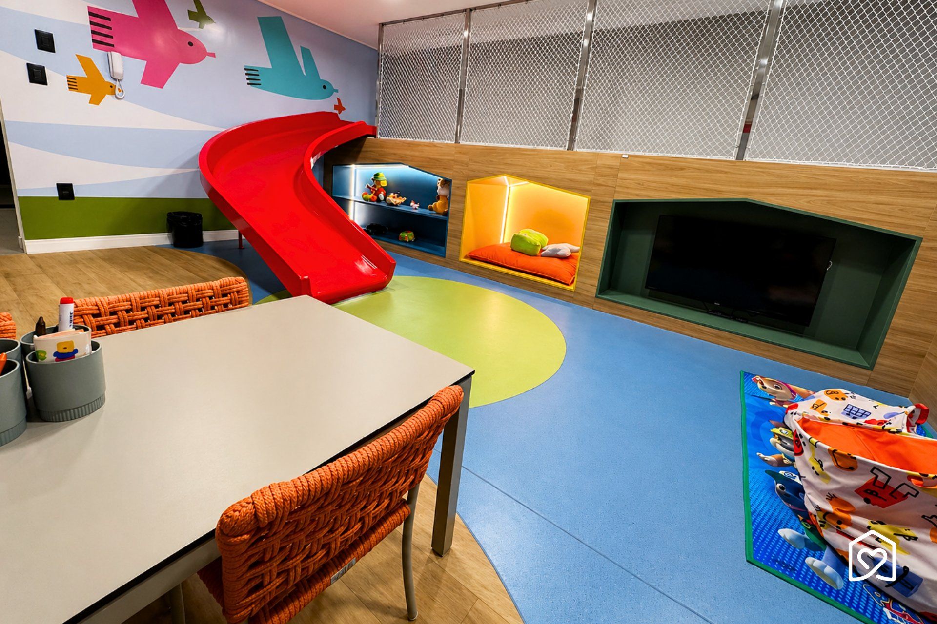 Un'area giochi per bambini con uno scivolo, tappetini e uno schermo televisivo.