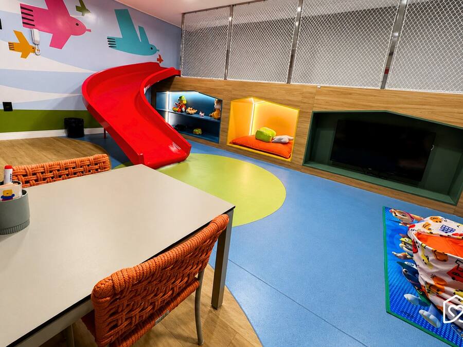 Ein Kinderspielbereich mit Rutsche, Spielmatten und einem Bildschirm.