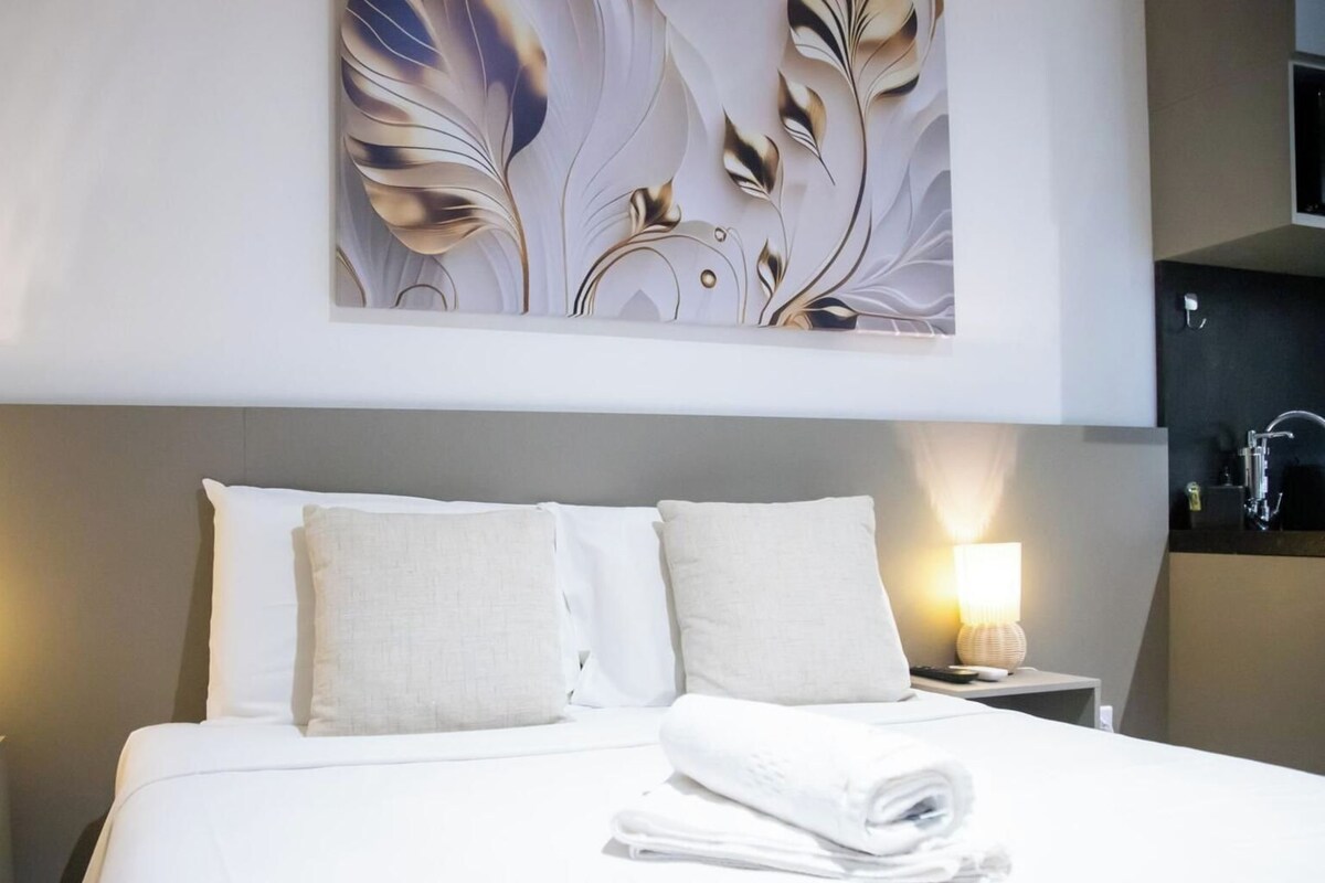 Una habitación de hotel con una cama, dos lámparas de noche, una obra de arte en la pared y una mesita de noche con lámpara.