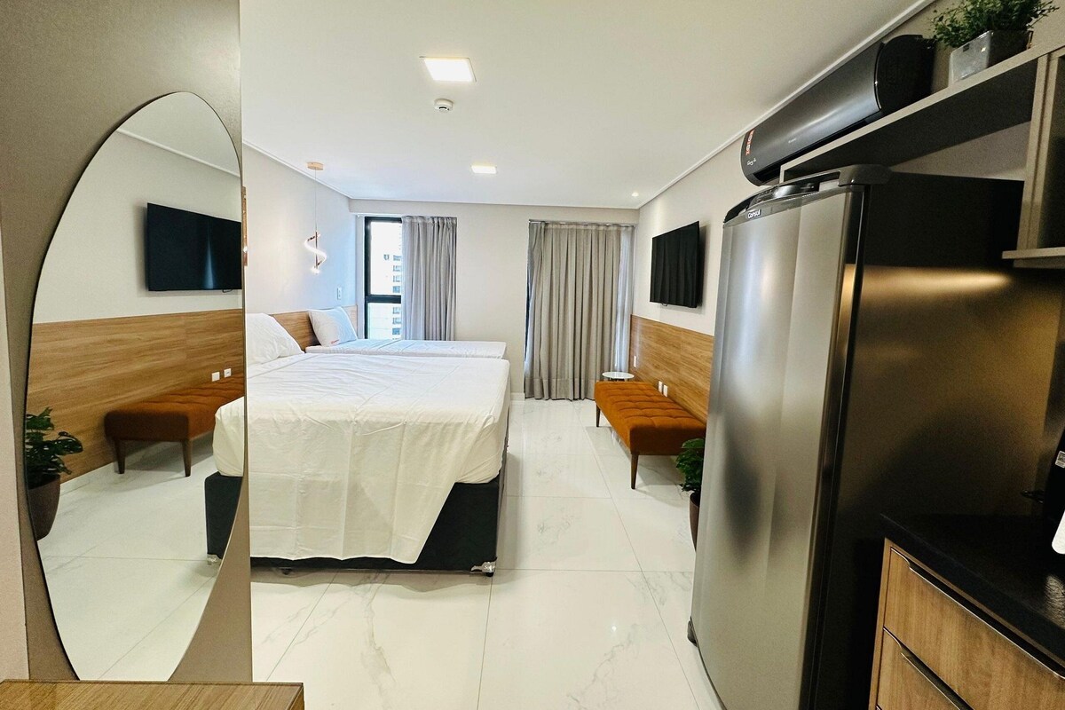 A hotel room with a bed, a sofa, a TV, a refrigerator, and a mirror.