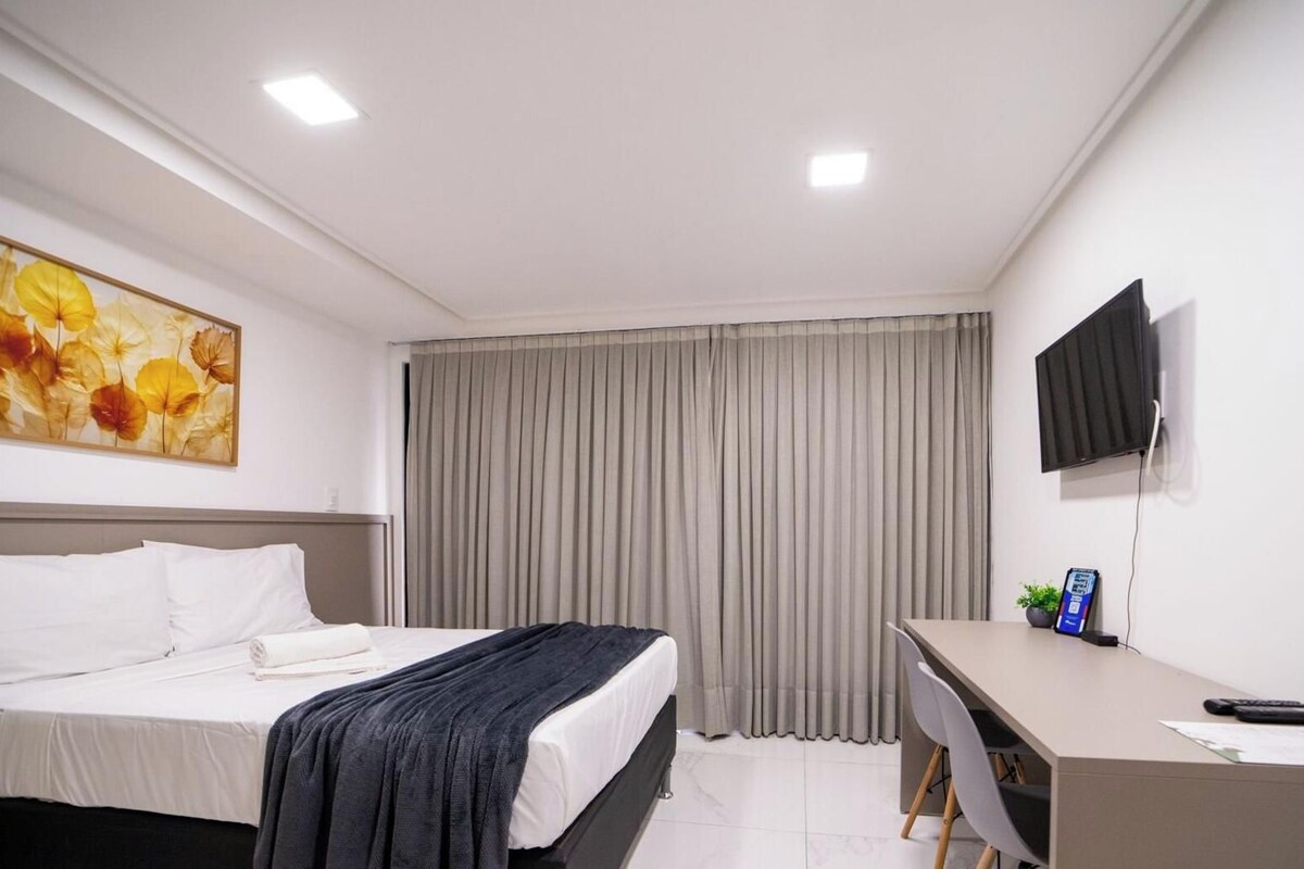 Habitación de hotel con cama, escritorio, televisor y ventana con cortinas.
