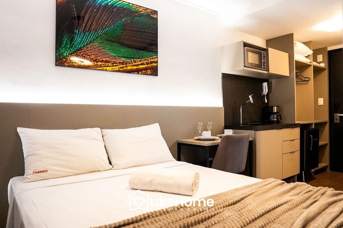 A hotel room with a bed, a small desk with a microwave, a coffee maker, and a TV.