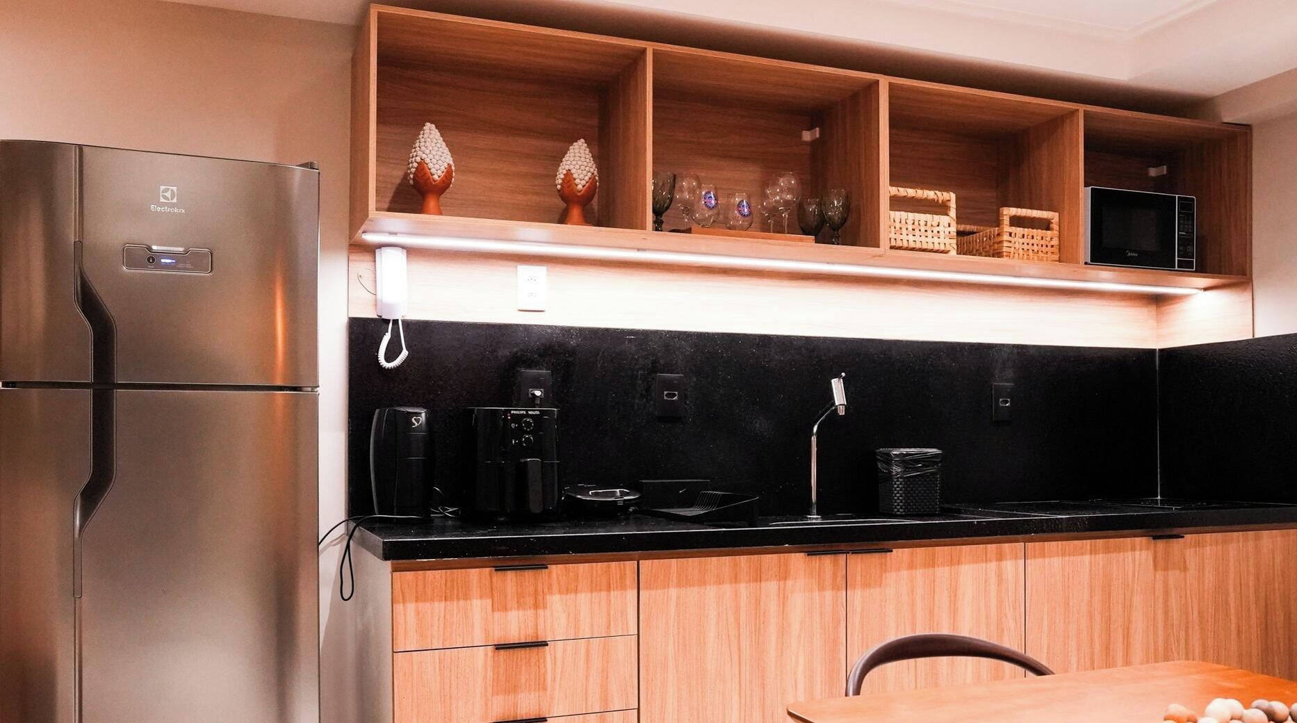 A modern kitchen with a stainless steel refrigerator, black countertop, wooden cabinets, and a microwave.
