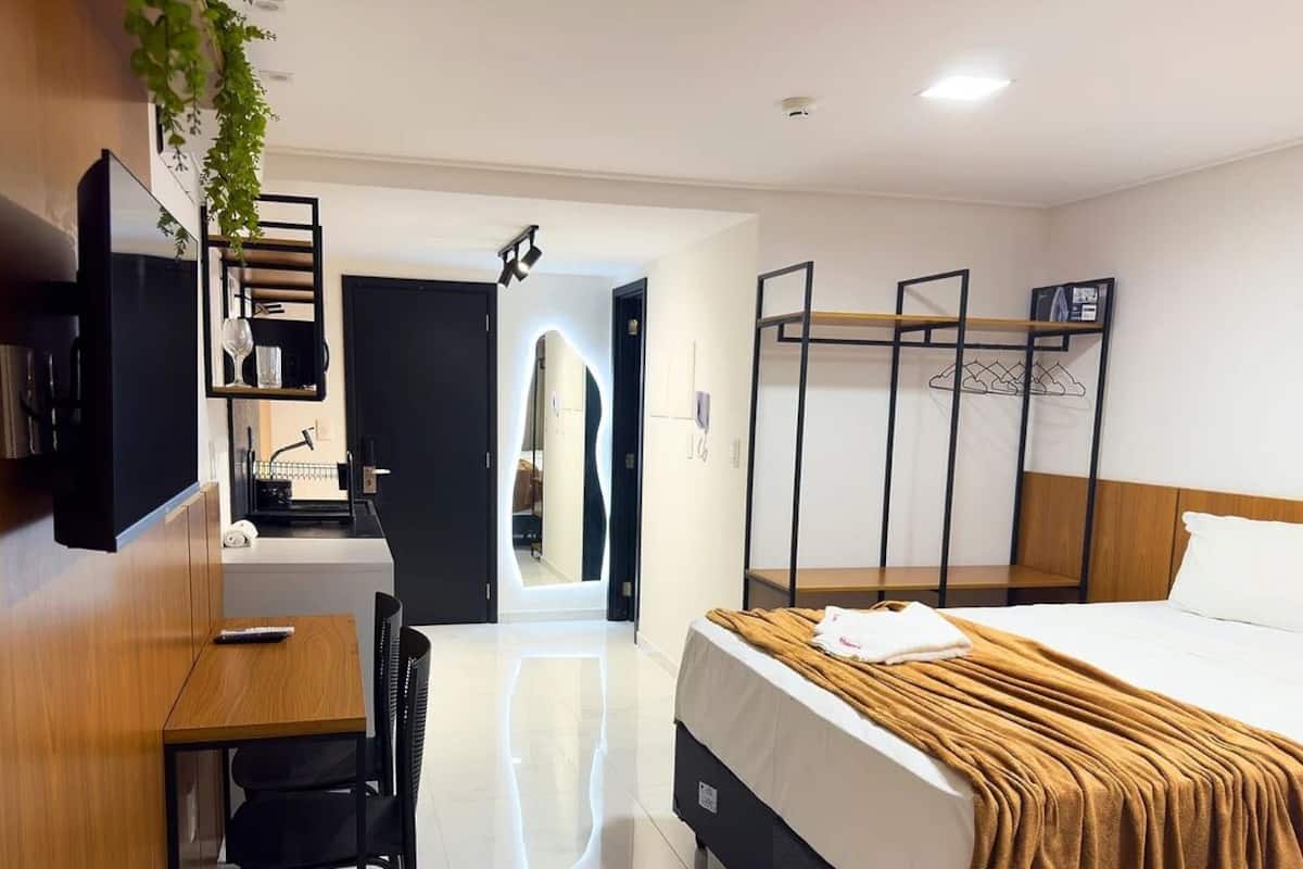 A hotel room with a bed, a desk with a chair, a TV, a wardrobe, and a bunk bed.
