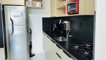 A compact kitchen with a stainless steel refrigerator, a microwave, a gas stove, and a sink.