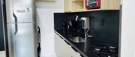 A compact kitchen with a stainless steel refrigerator, a microwave, a gas stove, and a sink.