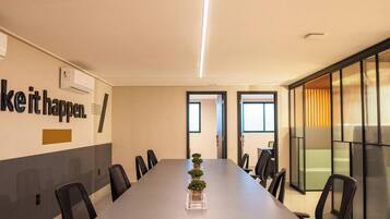 A conference room with a long table, chairs, a potted plant, and a motivational quote on the wall.