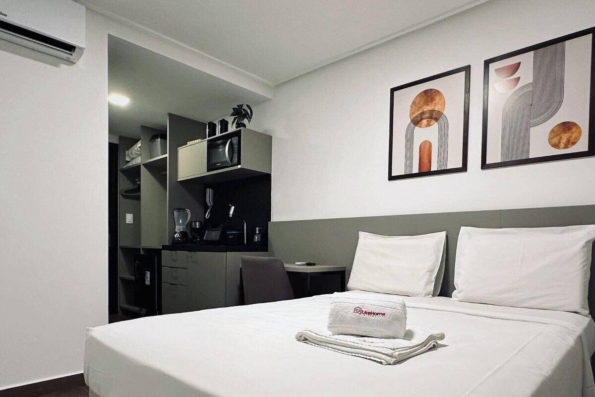 Habitación de hotel con cama, escritorio, silla, armario y dos obras de arte colgadas en la pared.