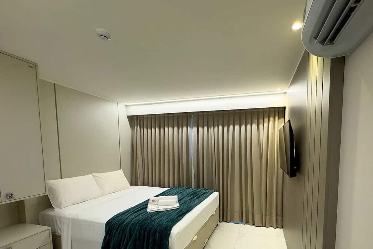 A modern hotel room with a bed, a flat-screen TV, and an air conditioning unit.
