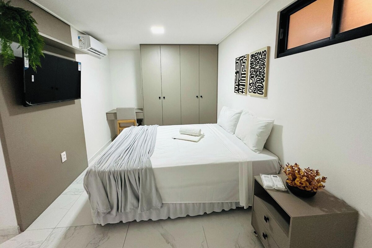 Habitación de hotel con cama, mesita de noche, armario y televisor montado en la pared.