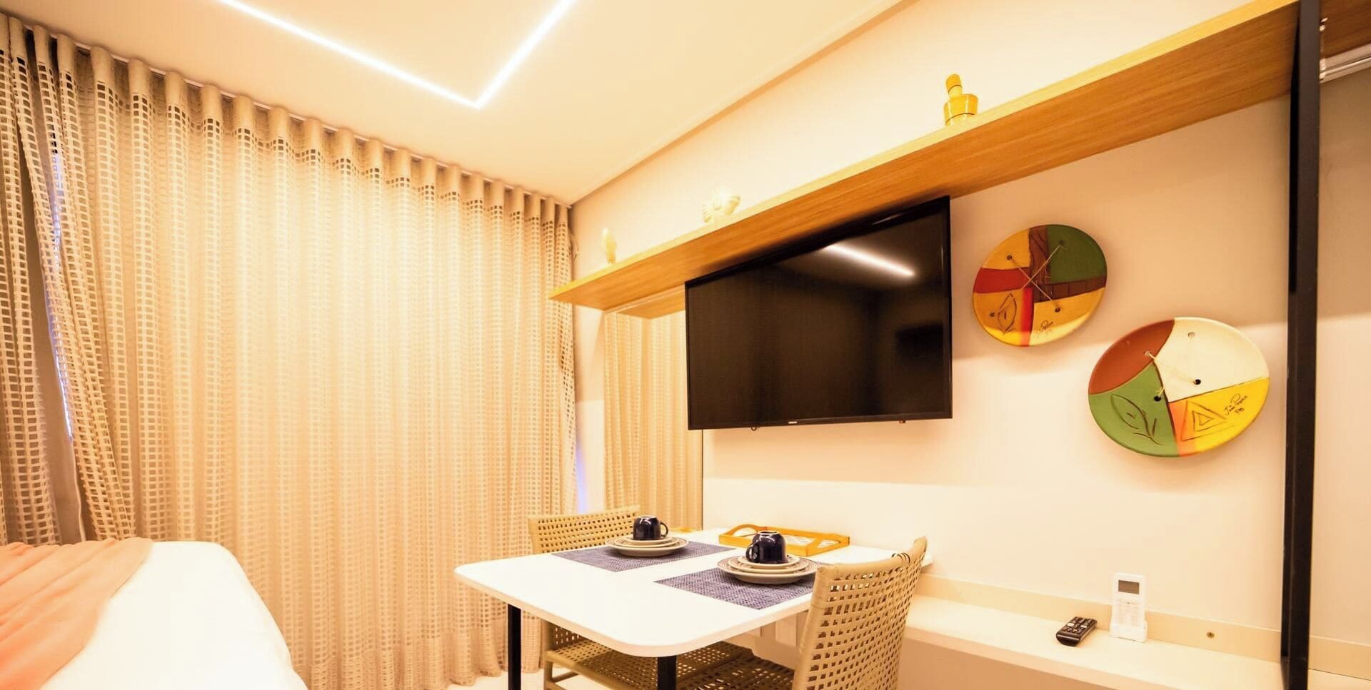 A hotel room with a bed, a table with a coffee cup, a TV, and wall clocks.