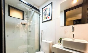 Un baño moderno con cabina de ducha de vidrio, inodoro y lavamanos con espejo.