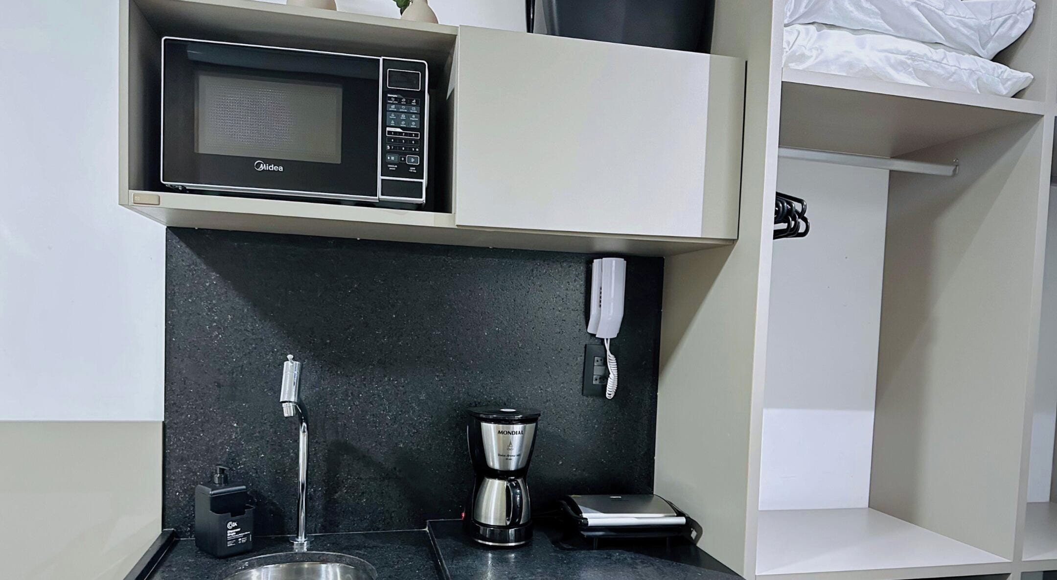 Ett litet kök med mikrovågsugn, kaffebryggare och en telefon.