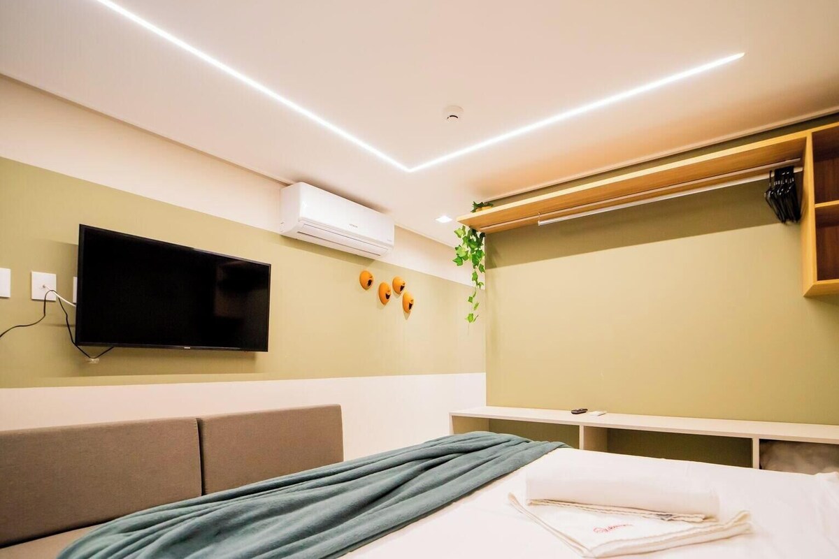 Una habitación de hotel moderna con una cama, un televisor de pantalla plana, un aire acondicionado montado en la pared y un estante de madera.