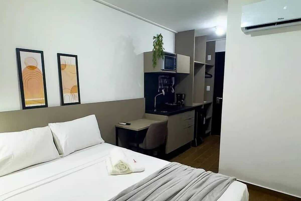 A hotel room with a bed, a desk, a chair, a small kitchenette, and two framed pictures on the wall.