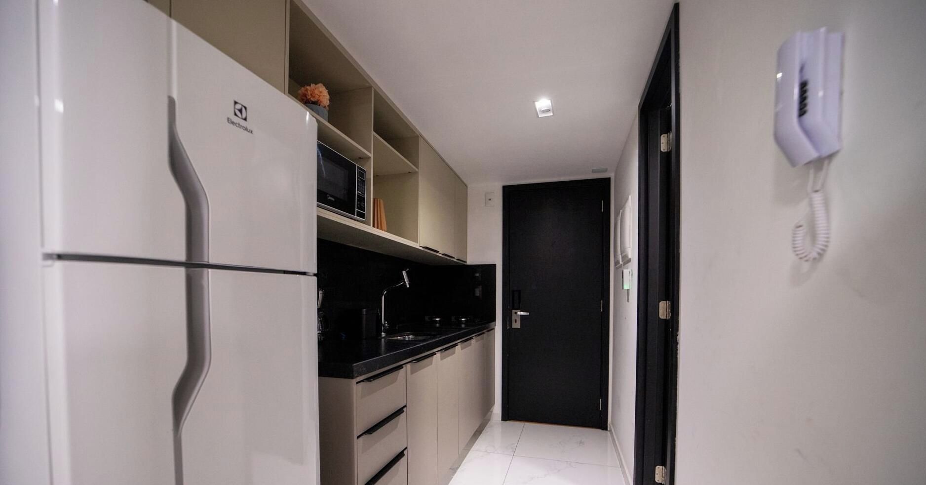 Un pasillo estrecho con un refrigerador, un microondas y un teléfono en la pared.