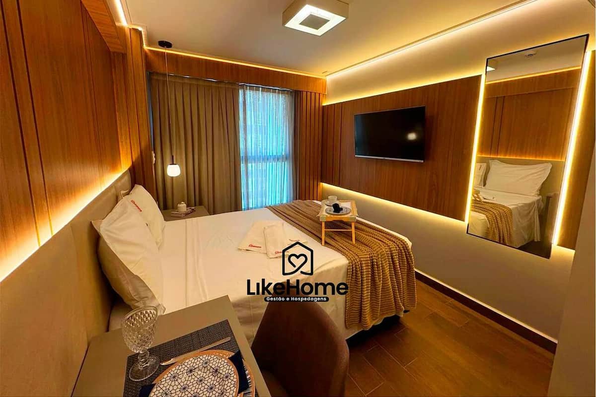 A hotel room with a bed, bedside table, lamp, and a large mirror.