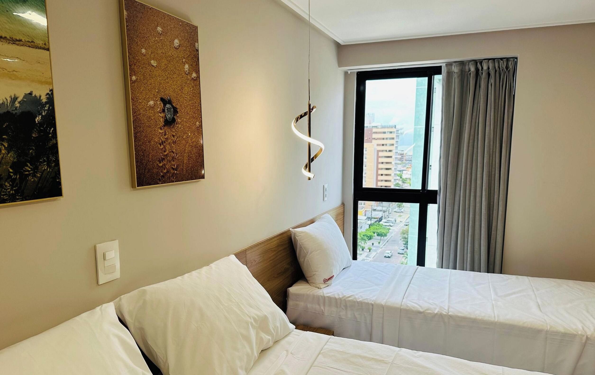 Habitación de hotel con dos camas, un ventanal con cortinas, una lámpara de pared y un cuadro.