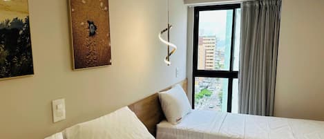 Une chambre d’hôtel avec deux lits, une grande fenêtre avec des rideaux, un luminaire fixé au mur et un tableau.