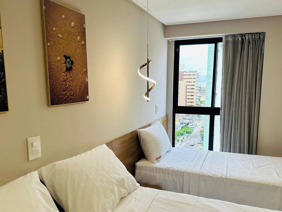 Une chambre d’hôtel avec deux lits, une grande fenêtre avec des rideaux, un luminaire fixé au mur et un tableau.
